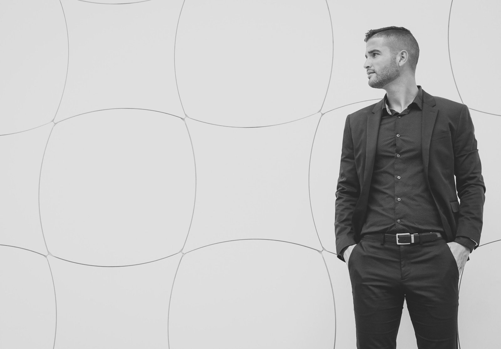 Black and white portrait of a confident man in a suit looking sideways against a geometric background.
